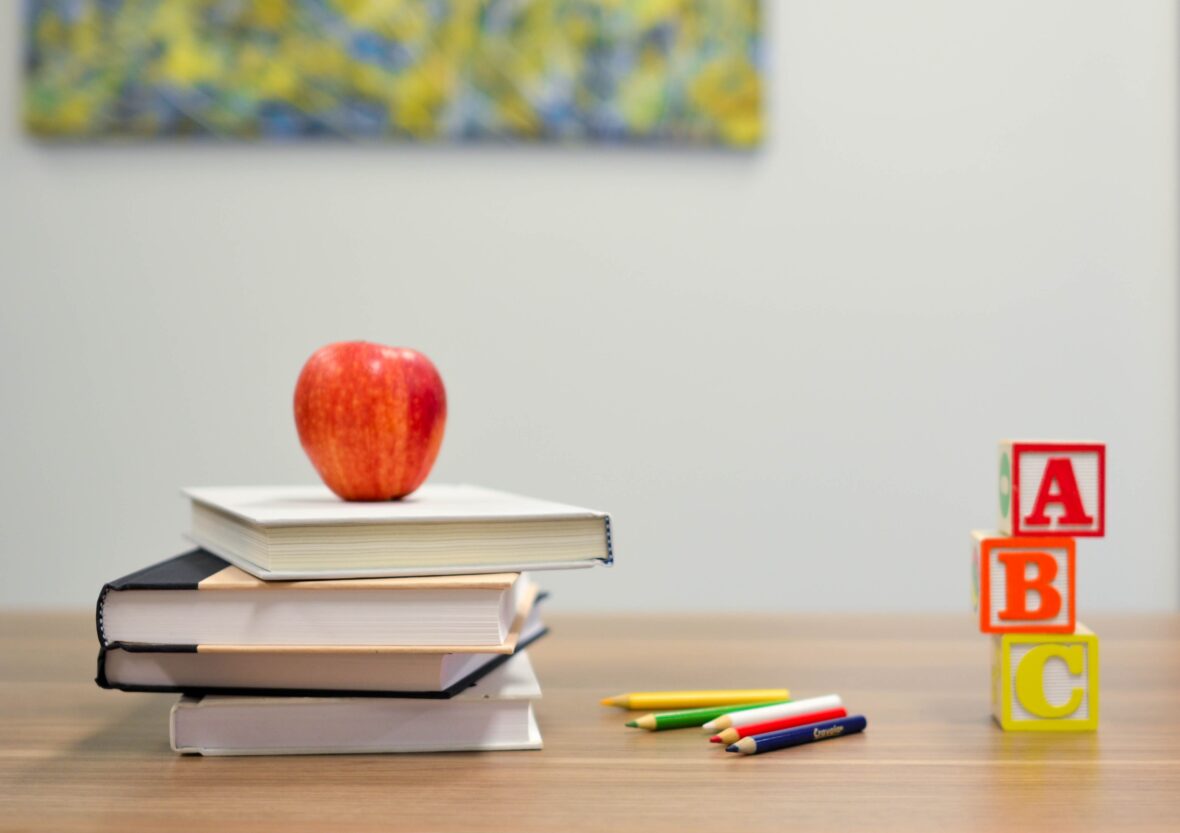 pino kirjoja, joiden päällä omena, kyniä ja kirjanpalikat pöydällä
